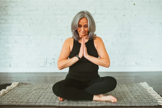 Joanna (Jo) in a peaceful prayer and namaste position on a yoga mat, silver hair, serene expression